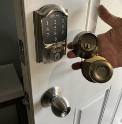 Hand holding brass door knobs next to a digital keypad lock installed on a white door