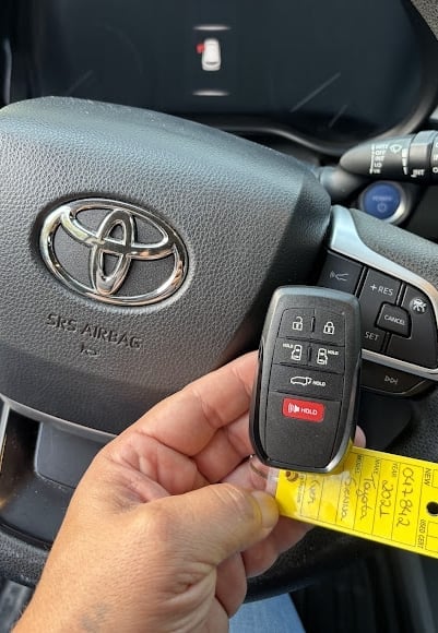 Hand holding a Toyota key fob inside a car with steering wheel visible in background