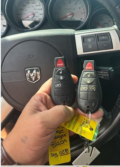 Hand holding two Dodge vehicle key fobs with yellow price tags inside a car dashboard